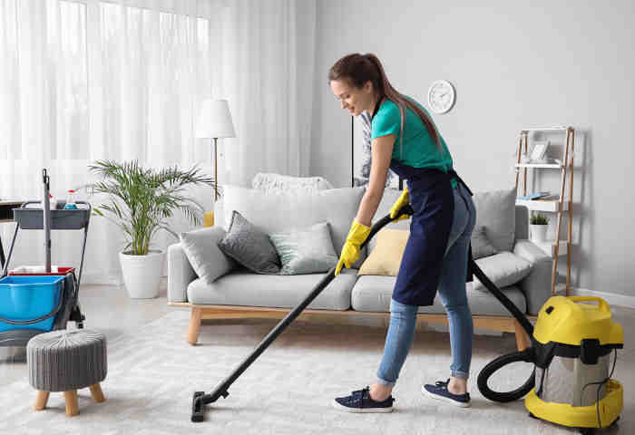 Female janitor with vacuum cleaner in room